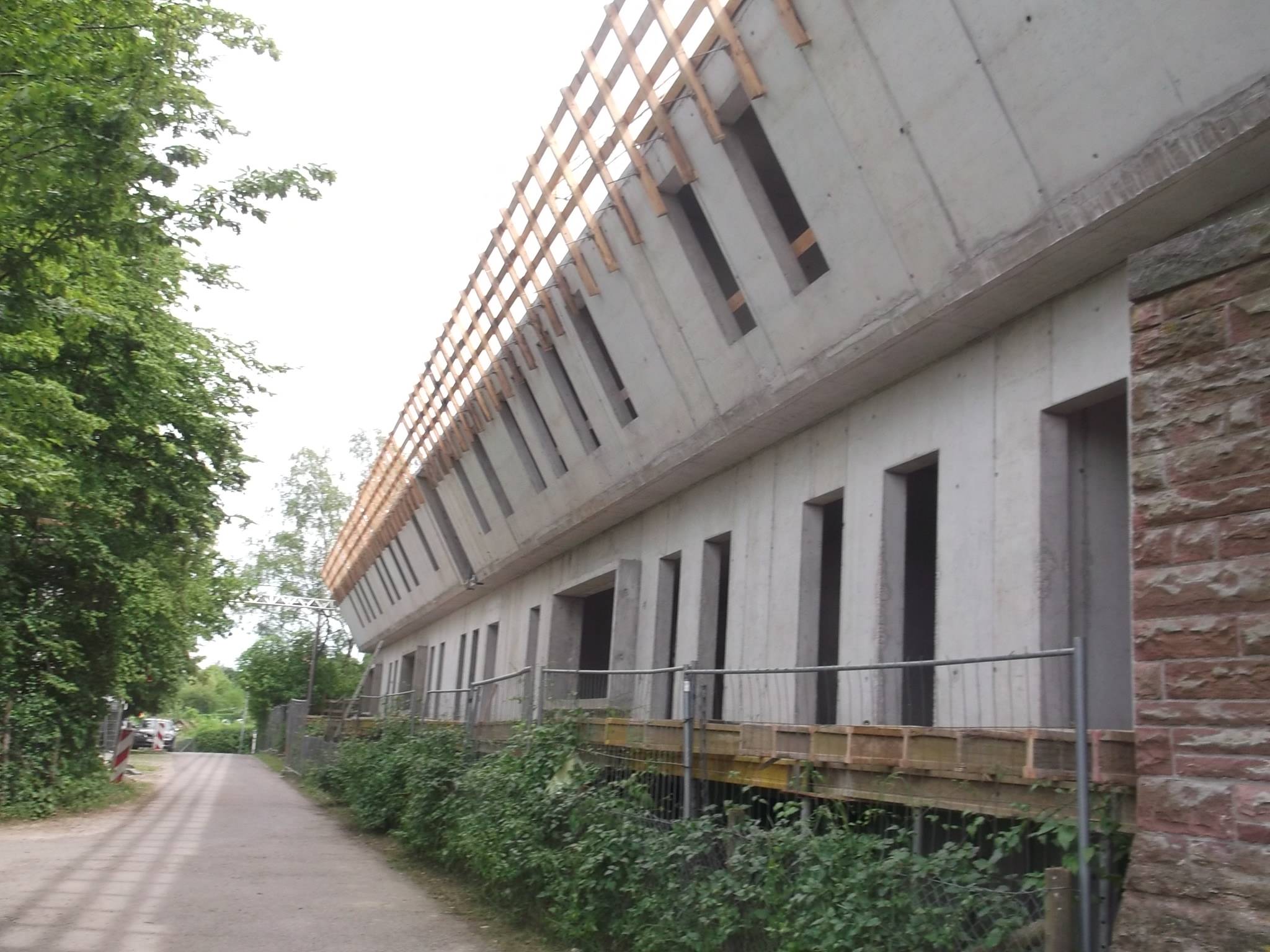 Rohbau Längsansicht — Betonfassade mit Fensteröffnungen und Holzsparren des gefalteten Dachs